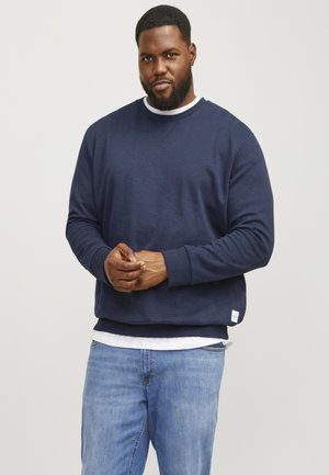Marineblauwe sweatshirt met een ronde hals en geribbelde manchetten, gecombineerd met lichtblauwe jeans. De sweatshirt heeft een klein label aan de zoom.