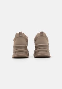 Zapatillas beige con un upper sintético liso, que presentan suelas gruesas y estriadas, además de lengüetas en el talón para facilitar el calzado.