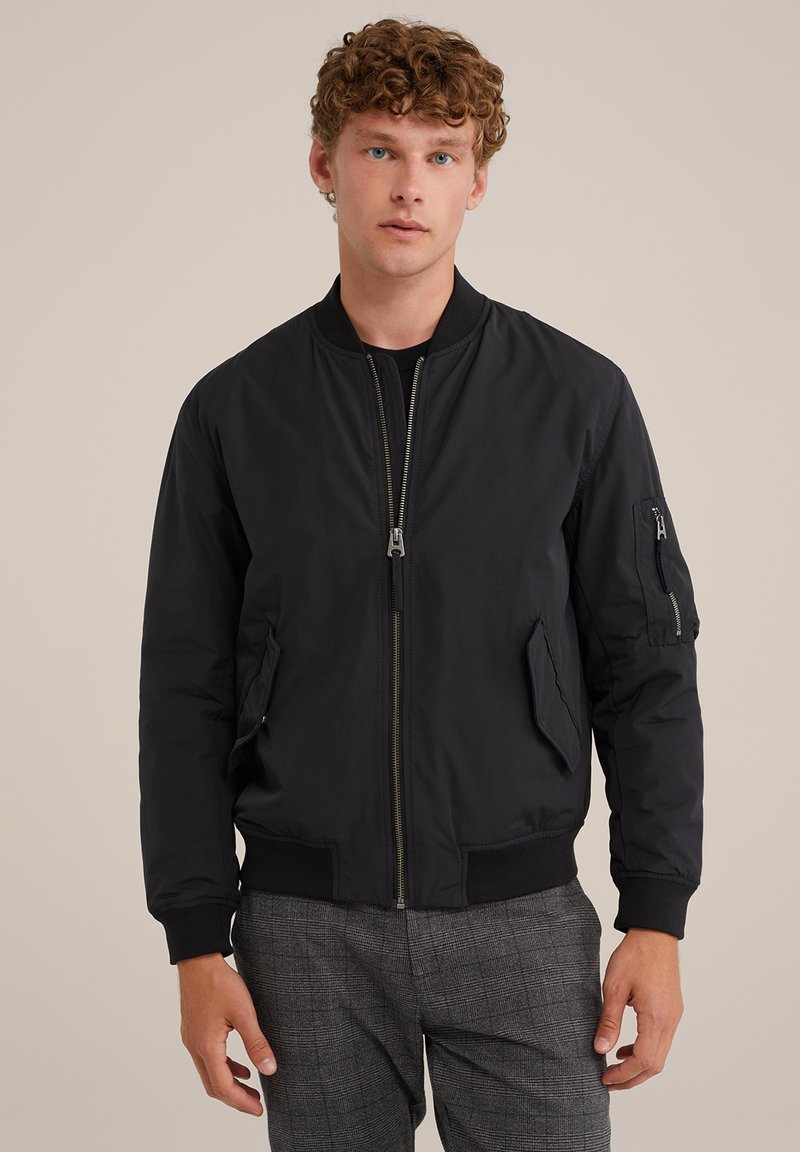 Černá bomber bunda se zipem vpředu, žebrovaným límcem a manžetami. Obsahuje dvě boční kapsy a kapsu na zip na rukávu pro praktické použití.