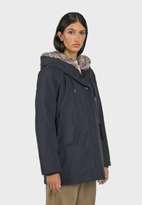 Veste parka bleu marine avec capuche en fourrure, fermeture à boutons sur le devant et poches latérales, offrant une coupe décontractée et une texture lisse.