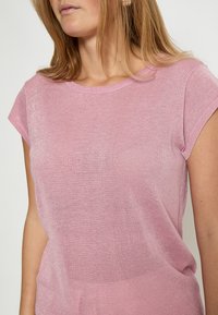 Top rosa a maniche corte realizzato in un tessuto lavorato a maglia leggero e testurizzato con un aspetto leggermente trasparente. Scollo rotondo e vestibilità casual.