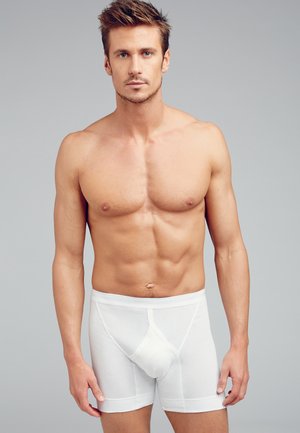 Hvide bomulds boxer briefs med frontlomme, elastisk livrem og en glat tekstur, båret af en model mod en neutral baggrund.
