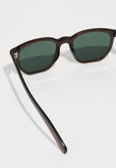 Ochelari de soare din plastic marron cu lentile nuanțate de verde, având o formă mai rotundă și temple elegante. Design curat, fără branding vizibil.