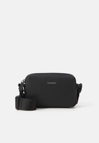Sac en bandoulière en cuir noir avec une finition texturée, fermeture zippée, sangle réglable et logo Calvin Klein à l'avant.
