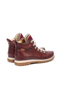 Bottines en cuir marron avec des accents en textile bordeaux, des lacets blancs et une semelle en caoutchouc robuste. Présente un logo sur le côté et un col rembourré.