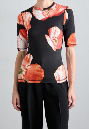 Person wearing a fitted black top with large orange and white poppy flower prints and black pants against a plain background.