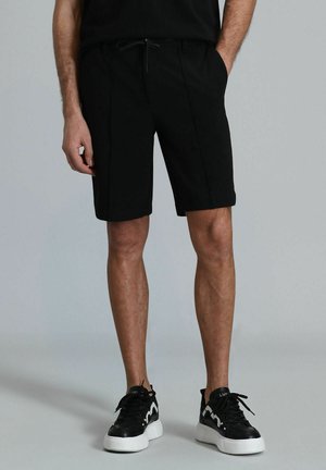 Shorts noirs à coupe décontractée, dotés d'une taille élastique et d'un cordon de serrage. Associés à des baskets noires avec des semelles et des accents blancs.
