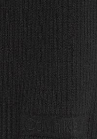 Sort ribstrikket stof i nærbillede med subtilt Calvin Klein-logo præget nær bunden i midten.