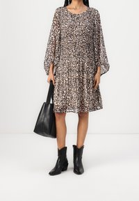 Woman wearing a long-sleeve leopard print dress, holding a black leather tote bag, and wearing black ankle boots with heels.