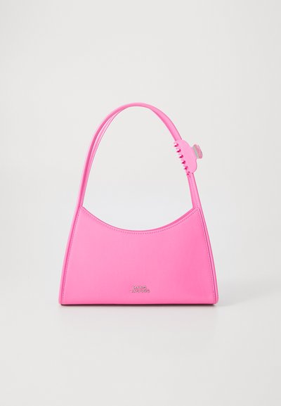 Sac à dos en cuir rose avec un haut arrondi, une forme solide et un petit détail accentué. Présente un logo discret à l'avant.