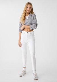 Šedý croptop svetr s výstřihem do V, bílé džíny s vysokým pasem a metalické stříbrné tenisky. Neformální design, volný střih a jemná textura.