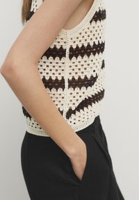 Virkat topp med öppen design som har växelvis mörkbruna och krämfärgade ränder. Matchas med svarta byxor, sidofickan synlig.