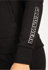 Zwarte sweatshirt met ribgebreide manchetten en tailleband. De linkermouw toont witte tekst "GORILLA WEAR" in vetgedrukte hoofdletters. Zachte stoffen textuur.