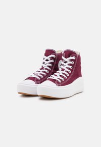 Para bordowych wysokich trampków z płótna z białymi grubymi podeszwami platformowymi i pasującymi białymi sznurówkami na jednolitym tle.