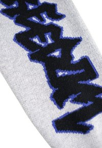 Grått tyg med stickad svart och blå stiliserad text. Mönstret har en djärv, grafisk design med en mjuk textur.