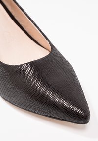Chaussure plate en cuir verni noir avec un bout pointu et une surface texturée irisée. Présente un dessus à coupe basse et une doublure intérieure lisse.