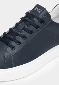 Sneaker in pelle blu navy con suola in gomma bianca, lacci piatti, punta rotonda e dettagli perforati vicino alla zona della punta. Logo impresso sulla linguetta.