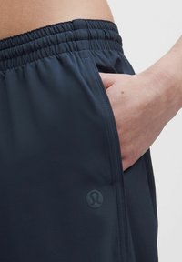 Mörkblå idrottsshorts med elastisk midja och sidoficka. Har en subtil logotyp på nedre benet och en slät yta.