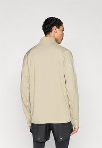 Μπεζ σακάκι μακρυμάνικο με ψηλό γιακά, με ανακλαστικές λεπτομέρειες στους ώμους, κατασκευασμένο από λείο, ελαφρύ ύφασμα.