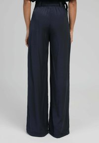 Pantalons à larges jambes en bleu marine, fabriqués en tissu lisse. Dotés d'une taille élastique et d'une silhouette fluide. Design minimaliste.