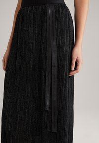 Černá plisé sukně s kovovým leskem, s hladkým pasem a ozdobnou stužkou s raženým textem na boku.