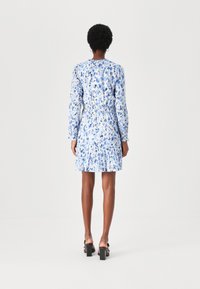 Blumenkleid in Hellblau und Weiß, mit langen Ärmeln, gerafftem Taillenbereich und plissiertem Rock. Glattes Material mit weicher Textur.