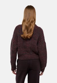Pull en tricot surdimensionné de couleur bordeaux foncé avec un motif texturé. Ourlet côtelé et manches larges, associé à un pantalon sombre à motifs.