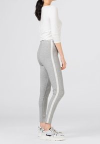 Grå leggings av stretchigt tyg med en vit sidenrand, kombinerade med en tajt vit topp och sportiga sneakers.