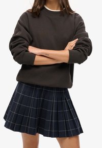 Sudadera gris oscuro con cuello redondo y puños acanalados combinada con una falda azul marino plisada con un patrón de cuadrícula blanca.