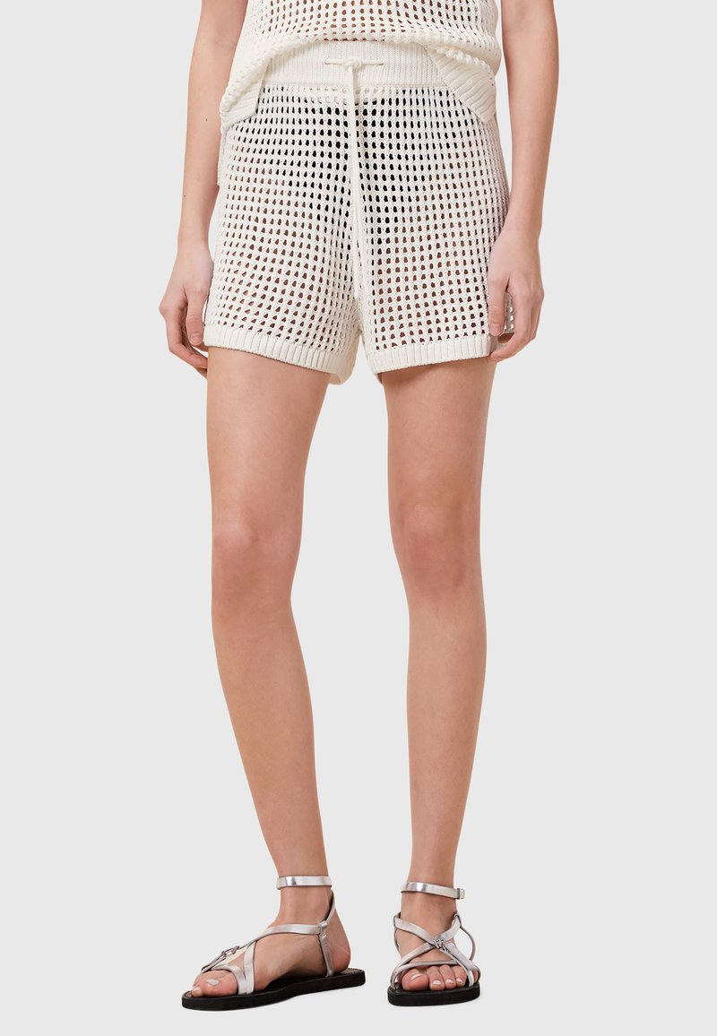 Hvide, strikkede shorts med en løs pasform, der har en snor i taljen og en netlignende tekstur, parret med sølvfarvede sandaler med stropper.