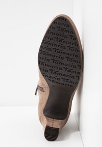 Bottine en daim beige à talon carré montrant le motif de la semelle embossé avec "Tamaris" et la taille 37 marquée près du talon.