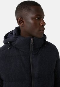 Granatowa pikowana kurtka wykonana z teksturowanej tkaniny, z wysokim kołnierzem, regulowanym kapturem oraz przednim zamkiem błyskawicznym z metalowymi elementami.