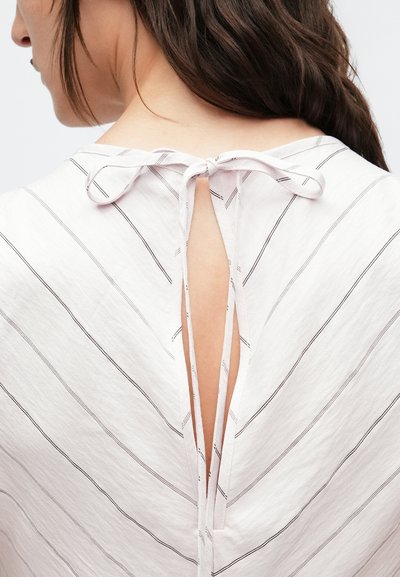 Biely vrchný diel z látky s čiernymi šikmými pásmi, s hlbokým výstrihom do V na chrbte a zaväzovaním na mašličku na zátylku. Jemná textúra.