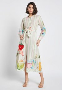 Leichtes, gestreiftes Hemdkleid in Pastellfarben, das strandthemed Drucke aufweist. Mit einem taillierten Gürtel und langen Ärmeln, kombiniert mit klaren High Heels.