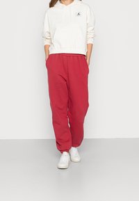 Röda träningsbyxor med elastiska manschetter, kombinerat med en krämfärgad hoodie med en svart logo på bröstet. Vita sneakers fulländar outfiten.