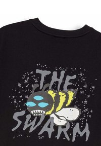 Tela negra con una abeja ilustrada que presenta tres ojos azules y dientes afilados, rodeada de pequeños insectos voladores y el texto que dice "LA COLMENA."