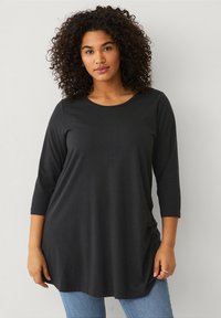 Zwarte lange mouwen tuniek top van zachte, rekbare stof met een ronde halslijn en een ontspannen pasvorm, gecombineerd met lichtblauwe jeans.
