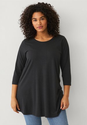 Zwarte lange mouwen tuniek top van zachte, rekbare stof met een ronde halslijn en een ontspannen pasvorm, gecombineerd met lichtblauwe jeans.