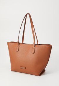 Sac fourre-tout texturé marron avec deux poignées, présentant un design minimaliste et une petite plaque logo à l'avant. Ouverture en haut sans fermeture.