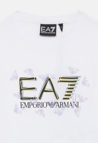 Balti medvilniniai marškinėliai su ryškia juoda ir aukso spalvos "EA7 EMPORIO ARMANI" logotipu, fone subtiliai matomos violetinės grafikos detalės.