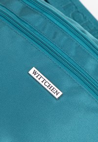 Borsa in tessuto turchese con una superficie liscia, chiusura con zip e una targhetta in metallo argentato con il marchio "WITTCHEN."