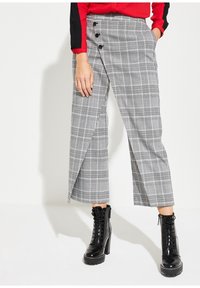Grijs geruite broek met een zijknopsluiting en een wijde pijpdesign, gecombineerd met zwarte veterschoenen tot de enkels. Glad stoffen textuur.