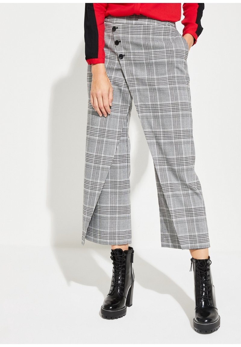 Grijs geruite broek met een zijknopsluiting en een wijde pijpdesign, gecombineerd met zwarte veterschoenen tot de enkels. Glad stoffen textuur.
