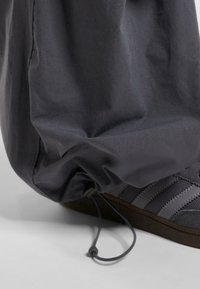 Grå sportsko med tre mørke striber, tekstureret overdel og gummisål, parret med grå, samlede stofbukser med en elastiksnor.