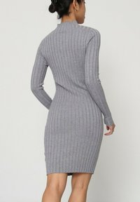 Robe tricotée côtelée grise avec des manches longues, un col montant et une silhouette ajustée. Présente des rayures verticales et un ourlet au niveau des genoux.