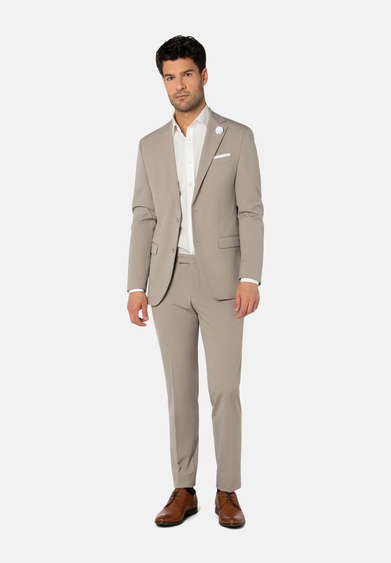 Licht beige pak met een getailleerd jasje, een wit overhemd en bruine schoenen. Het pak heeft een enkele borstzak en een subtiele textuur.