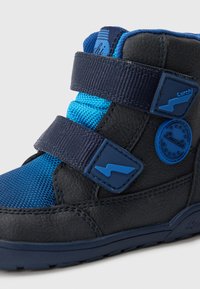 Blauwe en zwarte high-top schoenen van textuursynthetisch materiaal, met klitteband en cirkelvormig logo op de zijkant. Rubberen zool.