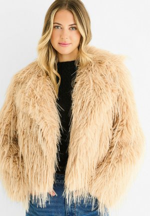 Faux fur cropped jacket in beige with long, soft strands, open front design, and large sleeves, worn over a black textured top.