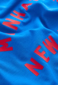 Tela azul con una textura suave que presenta letras rojas audaces que dicen "MANHATTAN NEW." No hay patrones adicionales ni detalles.