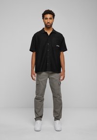 Black short-sleeve shirt with a front pocket and button-up design paired with light gray cargo pants and white sneakers.